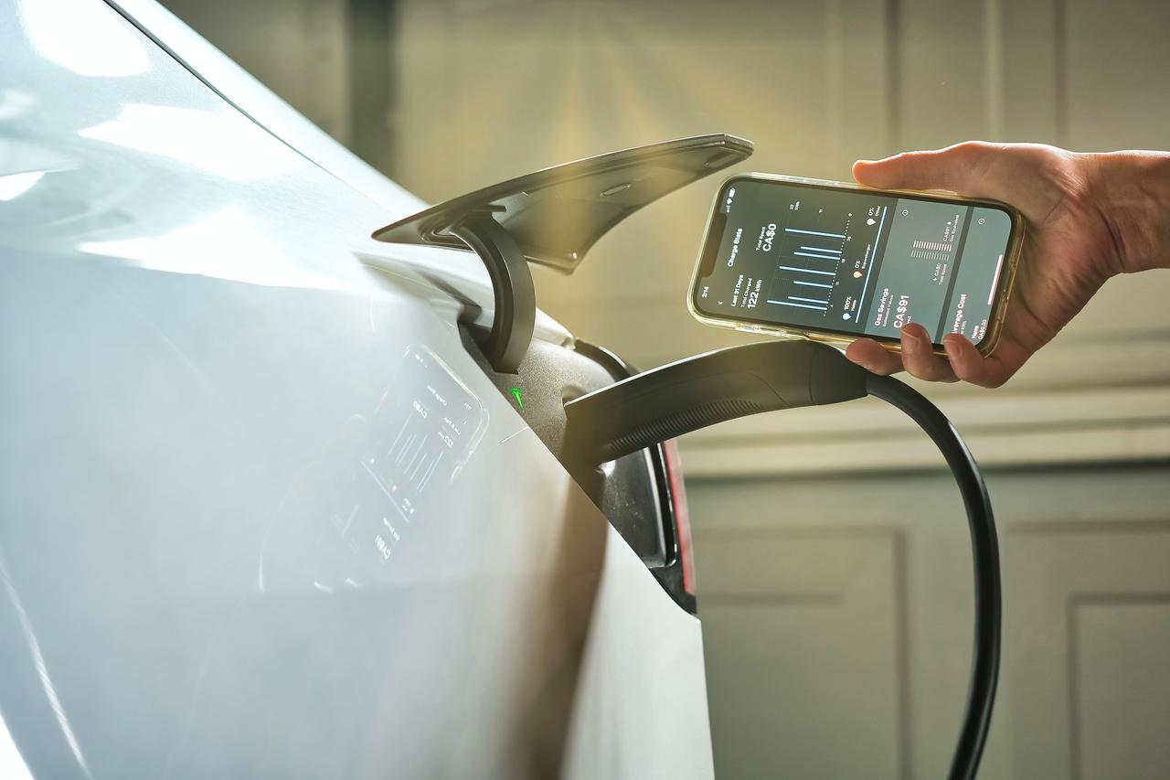 Elektroauto beim Laden mit Ladekabel während eine Smartphone App den Ladevorgang und Energieverbrauch anzeigt